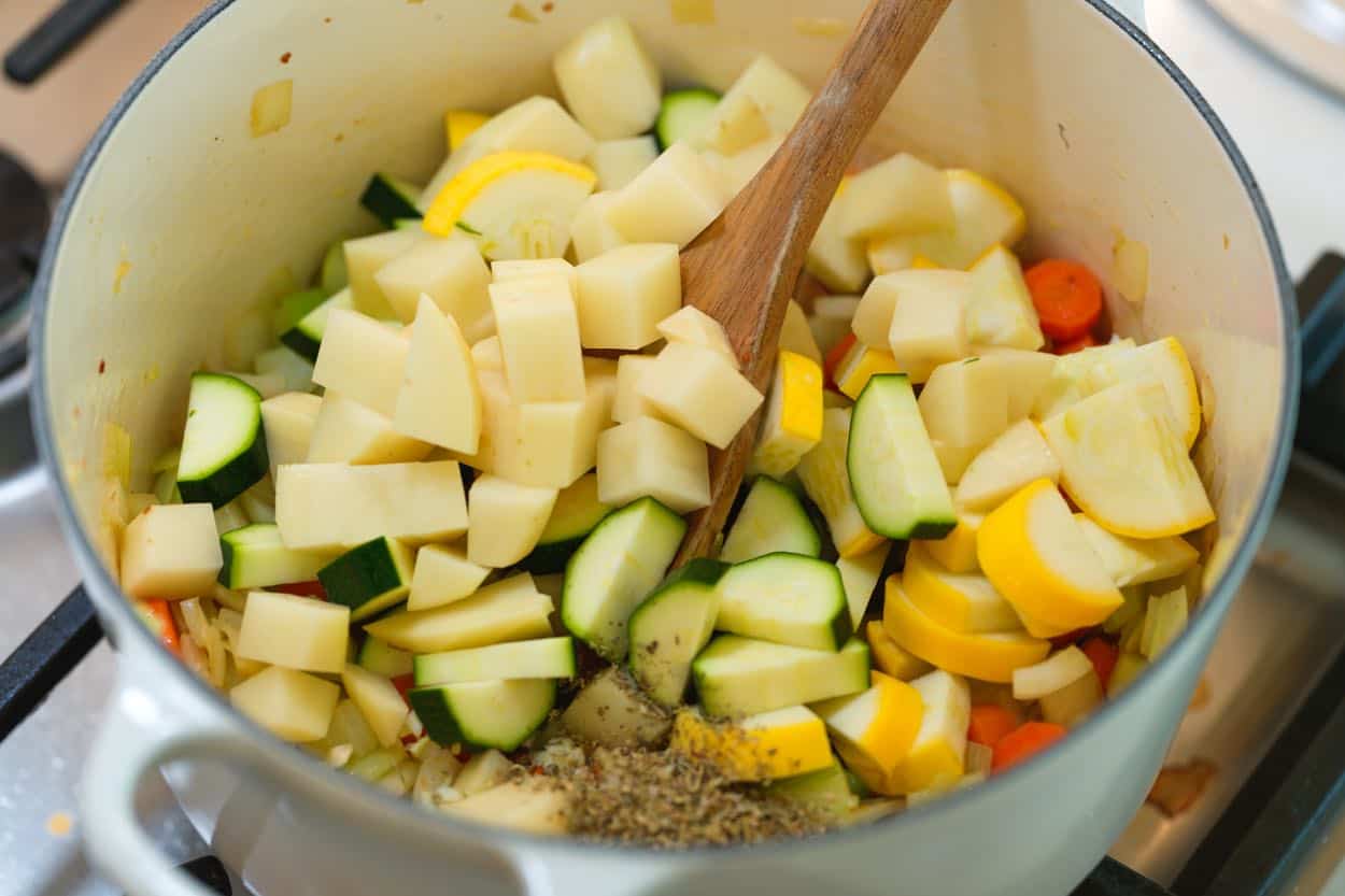 Česnako, itališkų prieskonių, bulvių ir cukinijų dėjimas į sriubos puodą