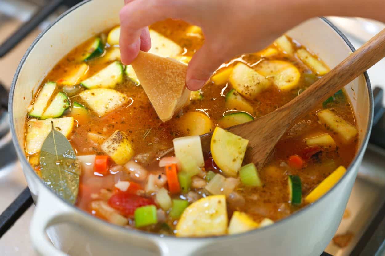 Parmezano žievės dėjimas į sultinį prieš troškinant.