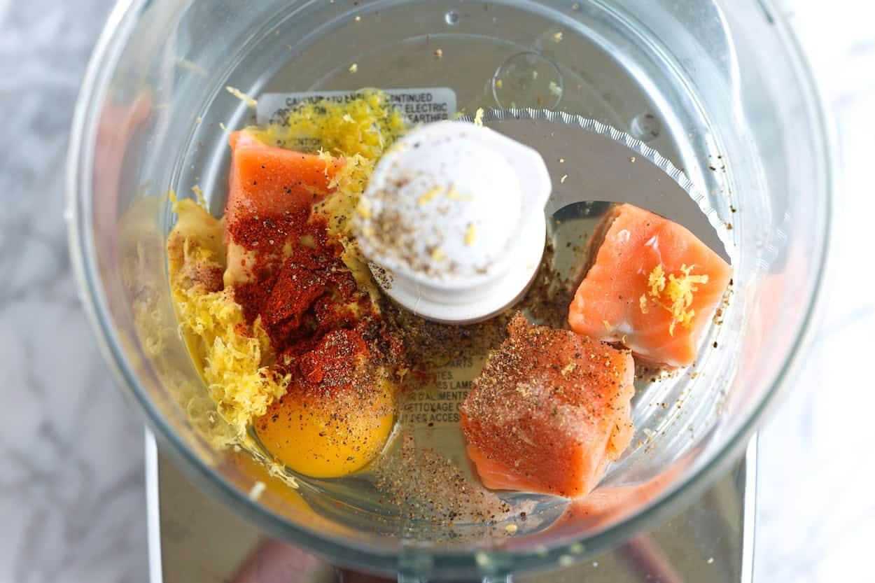 Šviežia lašiša, kiaušinis, garstyčios, citrinos žievelė ir prieskoniai virtuviniame kombaine, kad būtų pagamintas rišiklis lašišos burgeriams