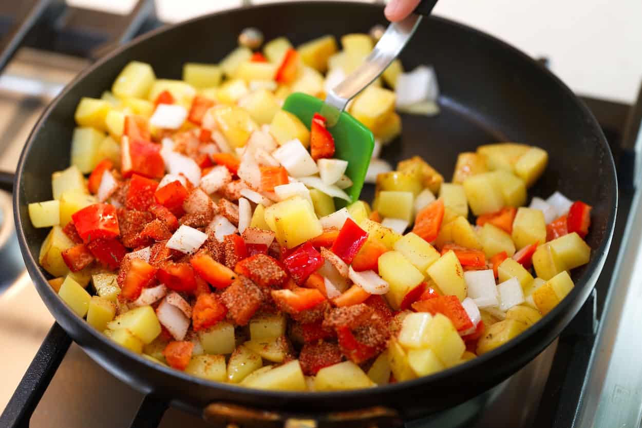 Prieskonių mišinio, saldžiosios paprikos ir svogūno maišymas į bulves keptuvėje
