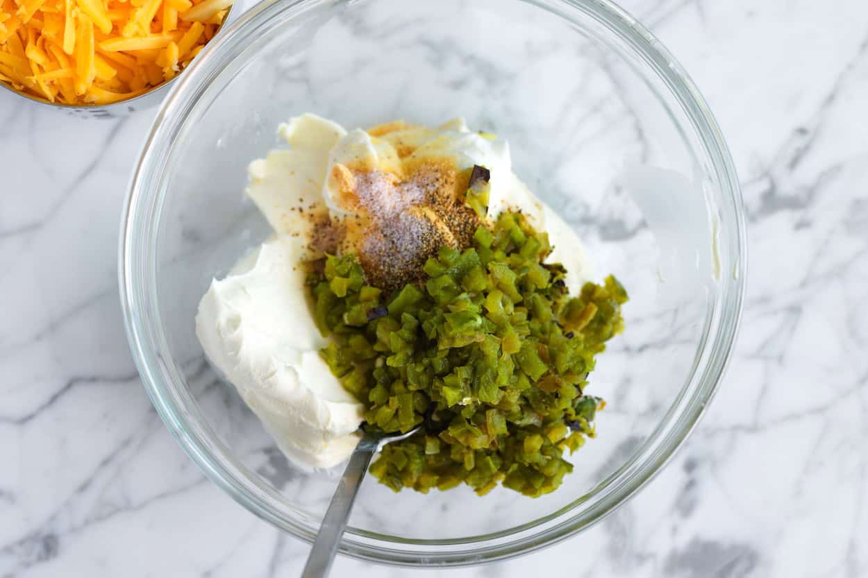 Smulkiai supjaustytų jalapeño pipirų ir žaliųjų svogūnų maišymas į kreminį sūrį padažui