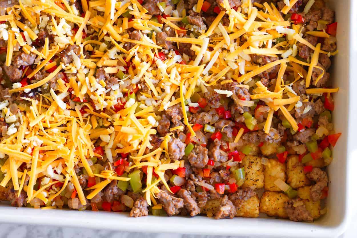 Layering sausage, onions, bell peppers, and cheese over tater tots for a breakfast bake.