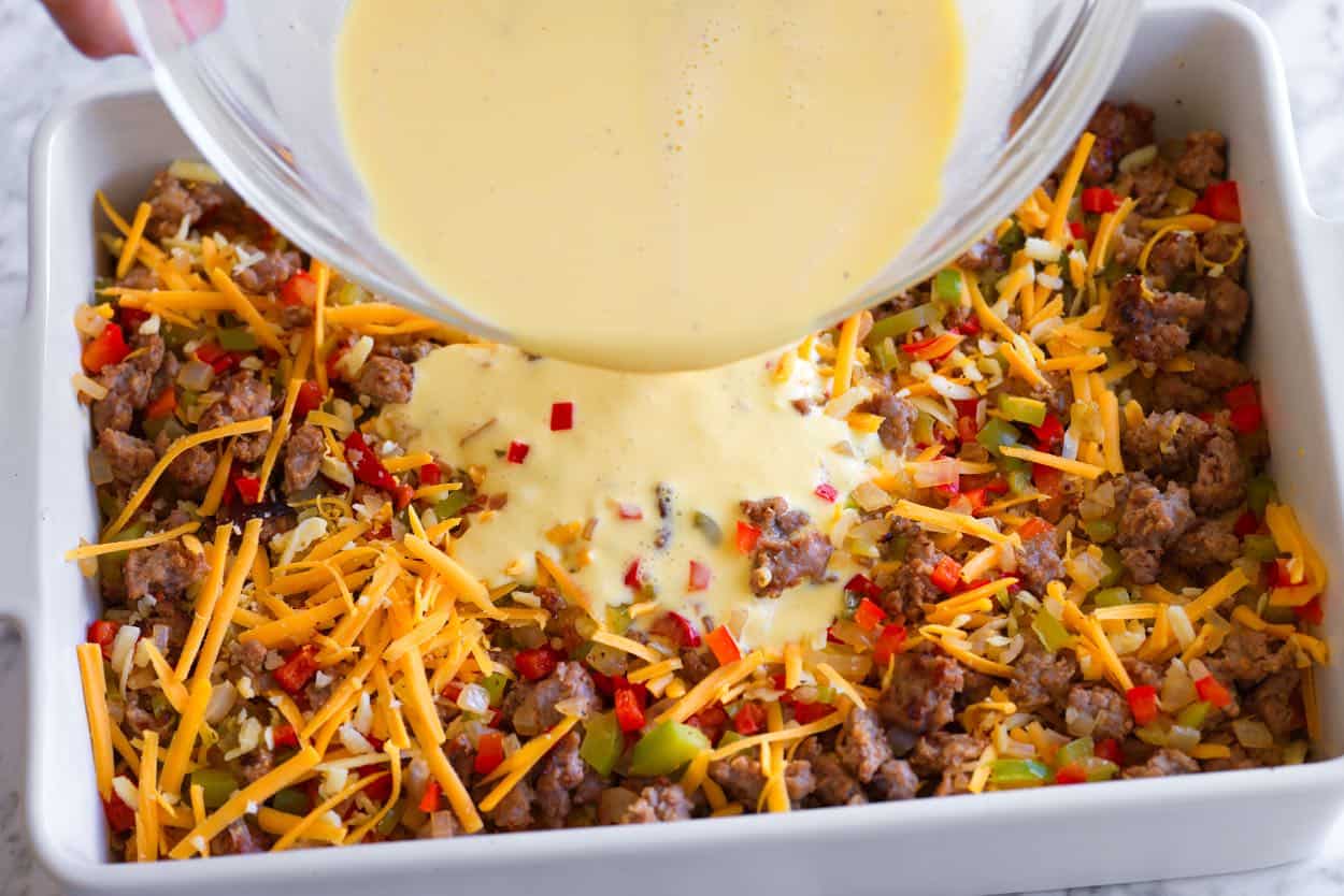 Pouring whisked eggs and cream over the sausage and tater tots before baking in the oven
