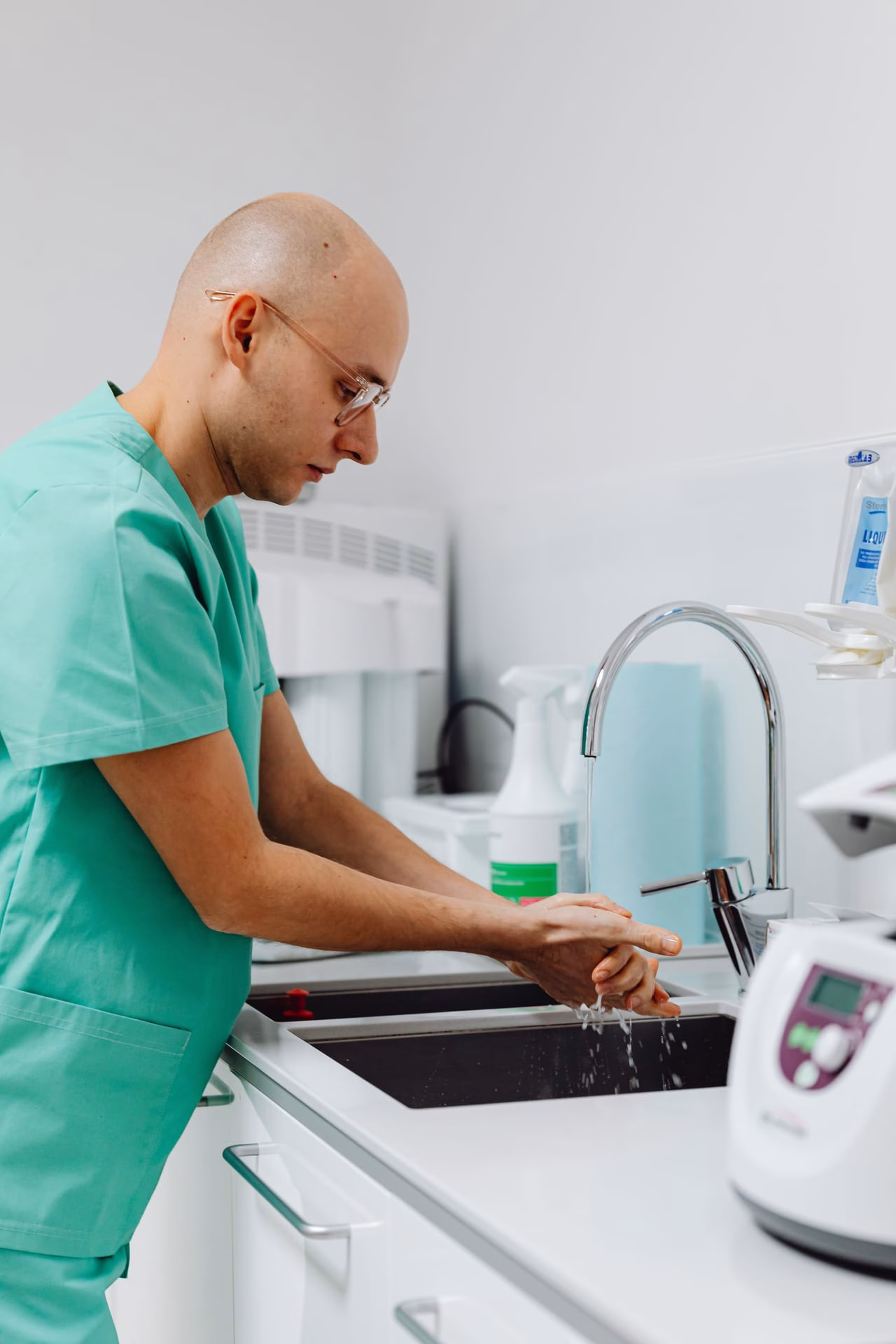 Doctor in scrubs practicing hand hygiene at a clinic sink.