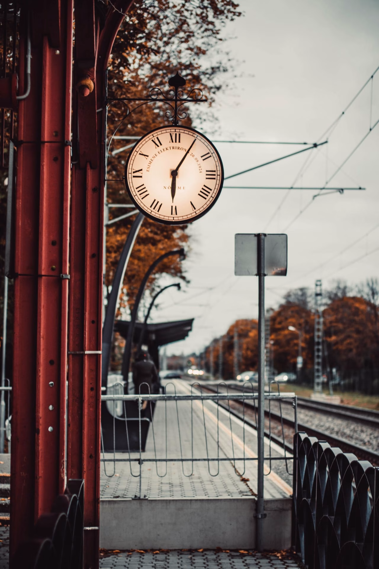 Antique clock at empty train station surrounded with trees in yellow foliage in cloudy autumn weather