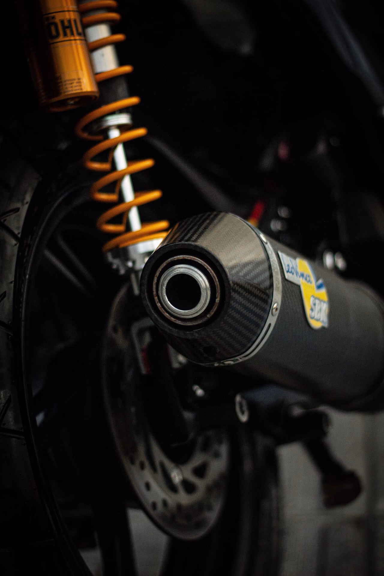 Detailed view of a motorcycle's exhaust and suspension system with a focus on the metallic parts.