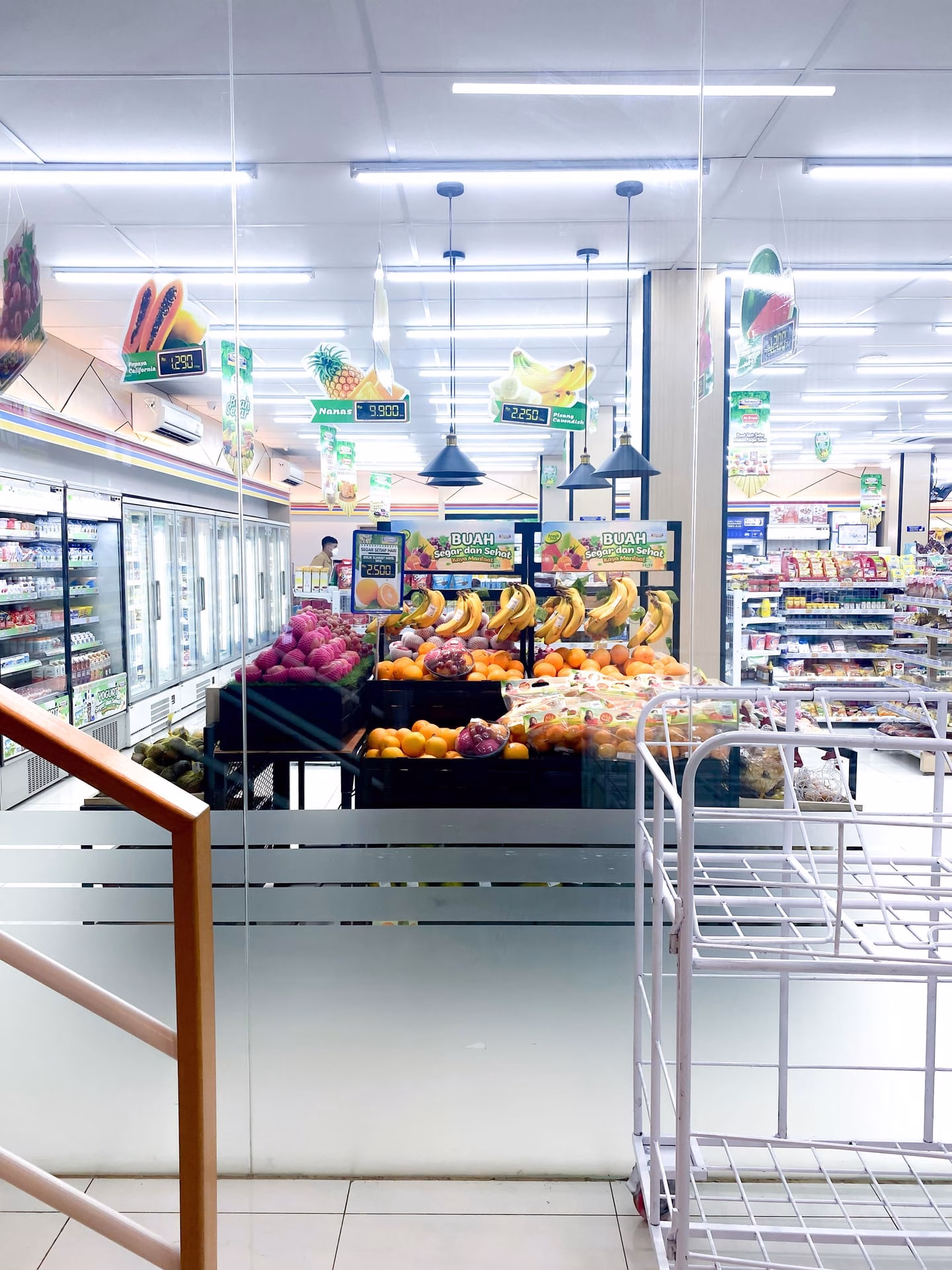 Vibrant fruit display in a well-lit supermarket aisle with fridges and shelves.