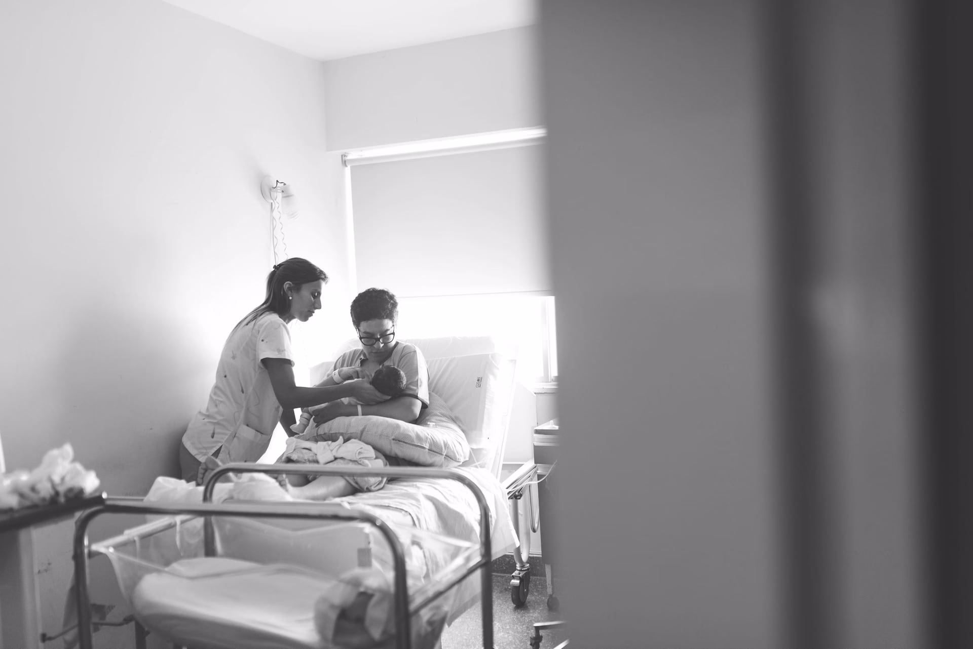 Black and white image of a nurse assisting a mother with her newborn in a hospital room.