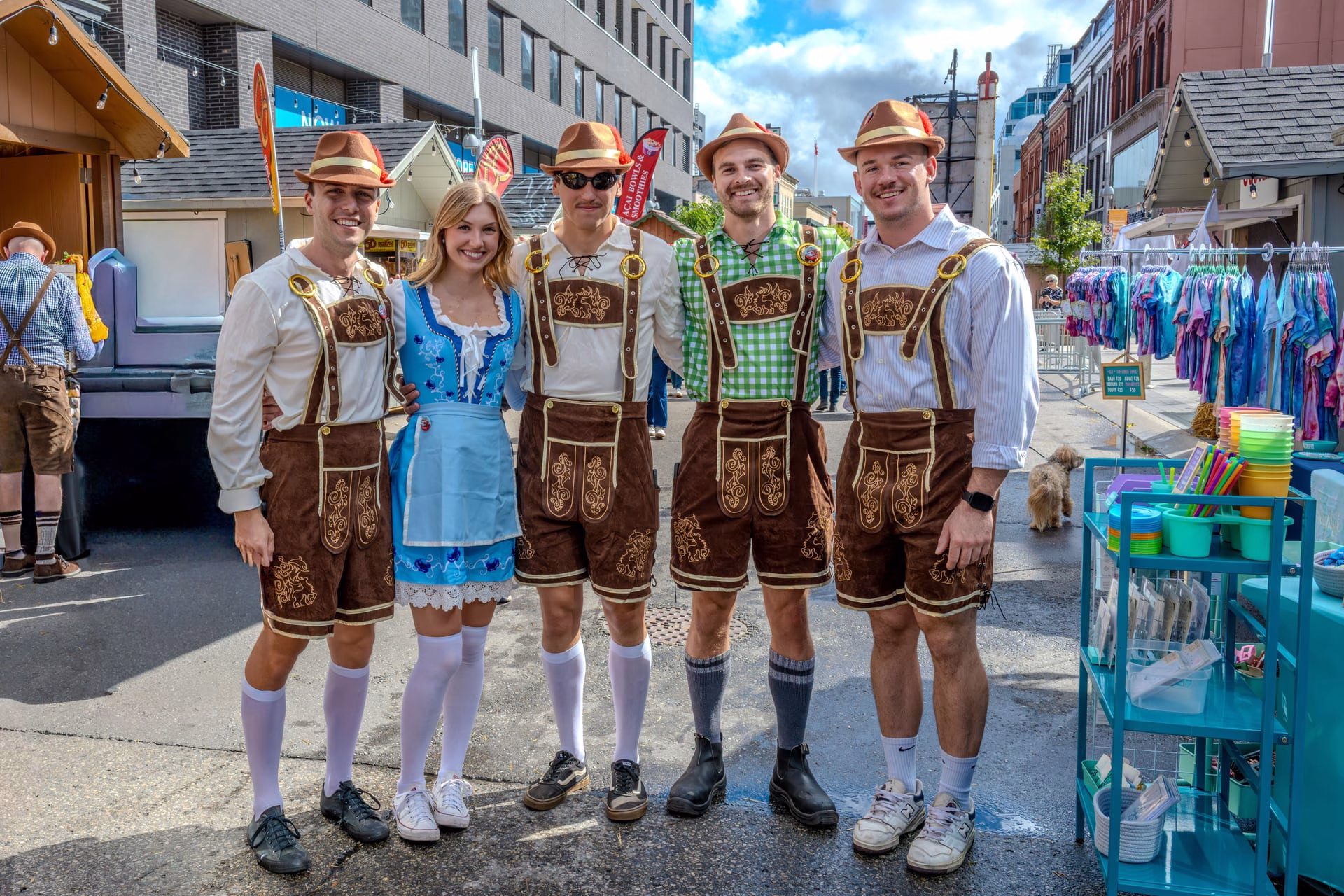 A group of adults in traditional German festival clothing outdoors, during a sunny day.