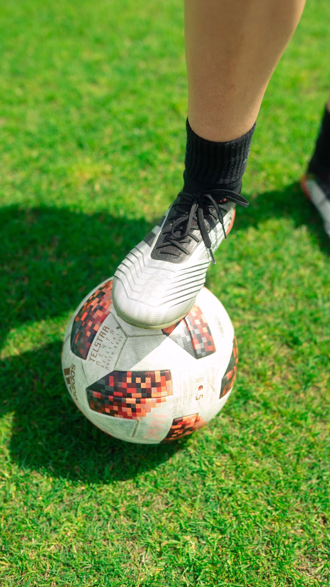 Close-up of a soccer player's foot on a ball on a lush green grass field.