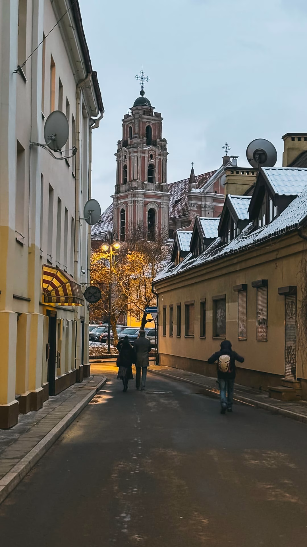 Picturesque view of Vilnius Old Town alley with church spire, evoking travel and winter exploration mood.