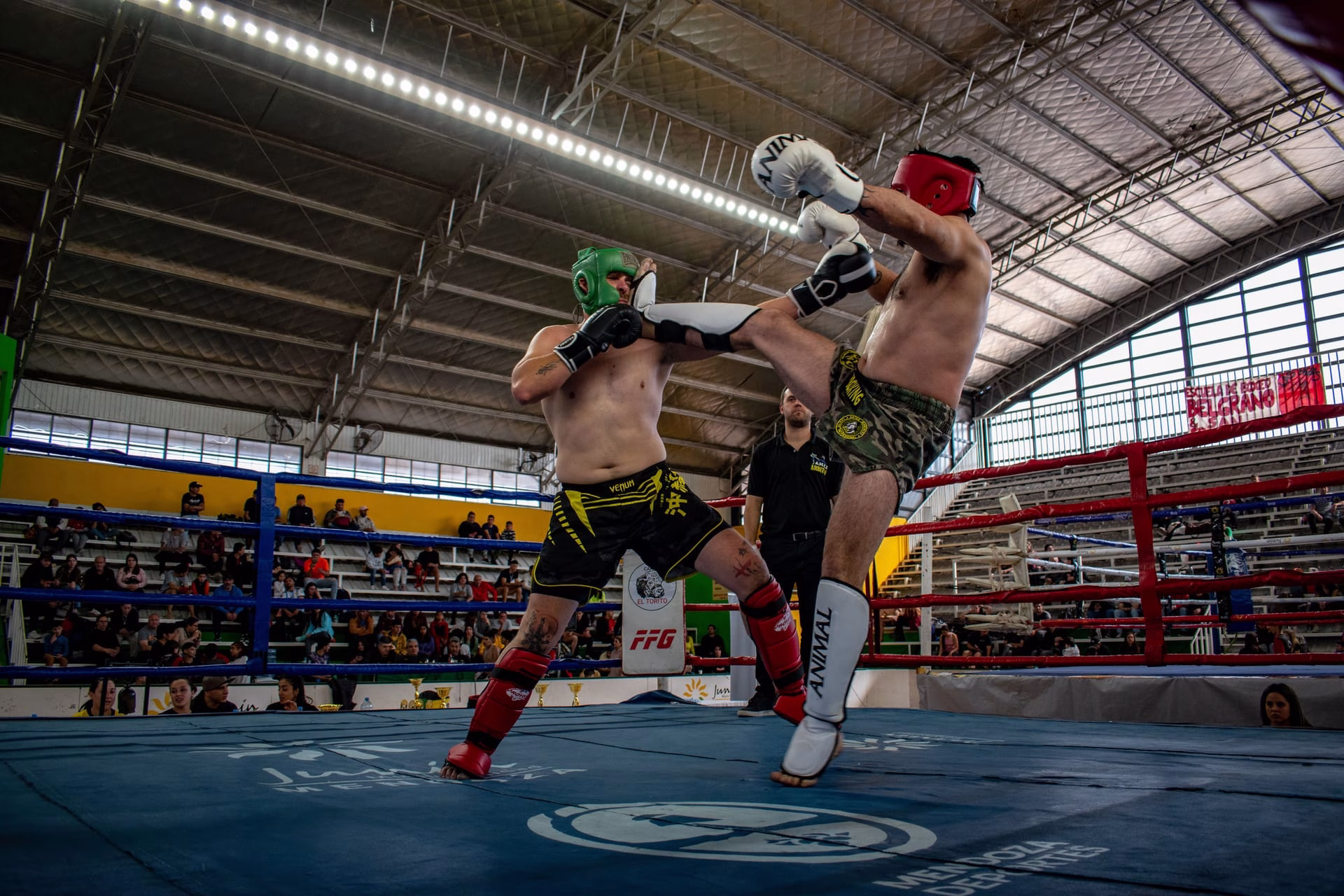 Intense kickboxing match between two male athletes in an indoor arena.