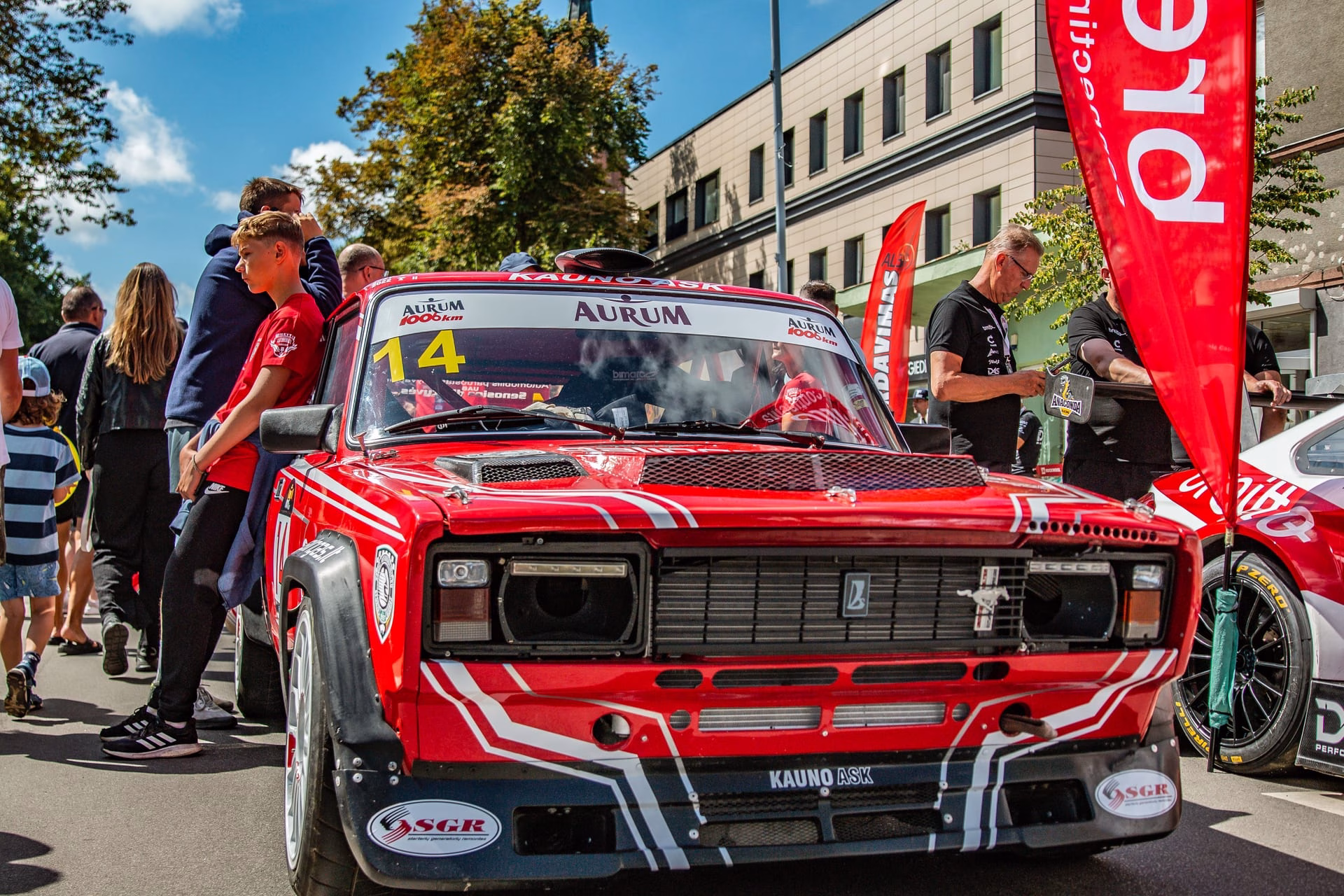 Exciting outdoor car racing event featuring a classic red race car and cheering audience.