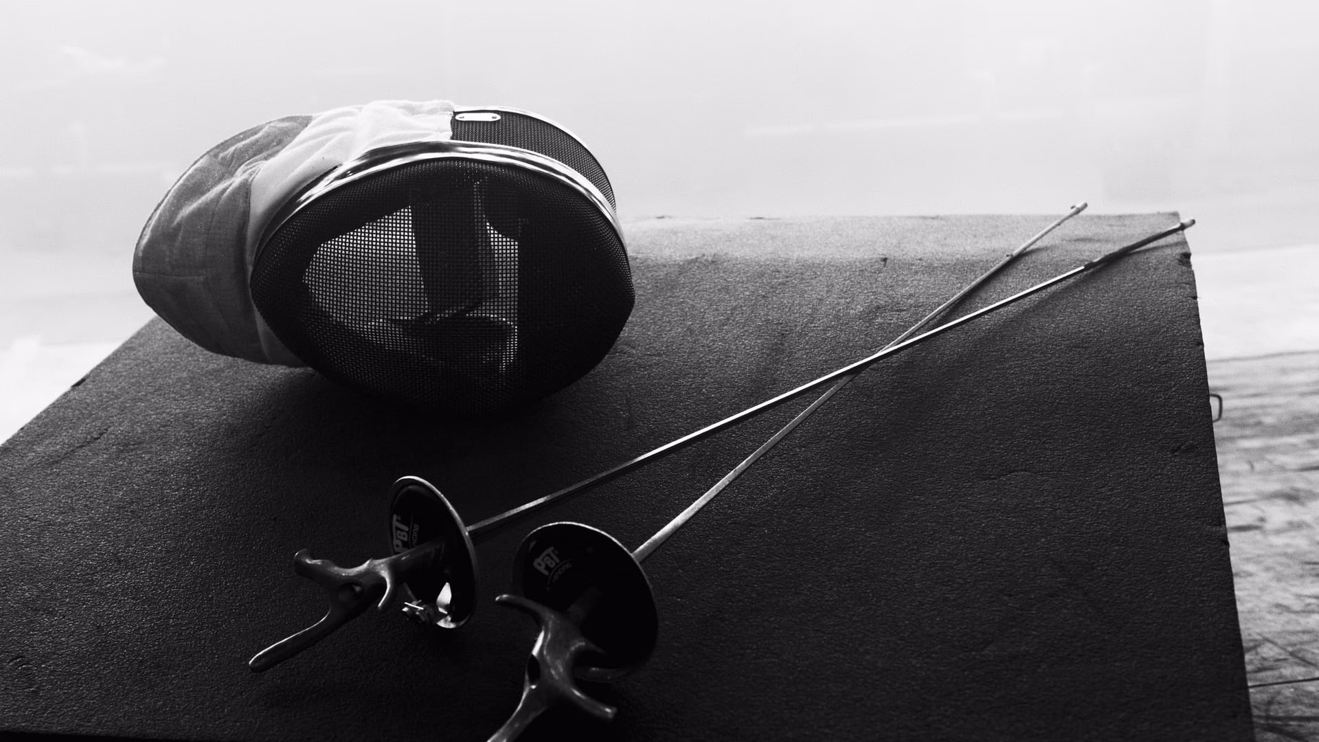 Close-up of a fencing mask and swords in black and white, showcasing a classic dueling style.