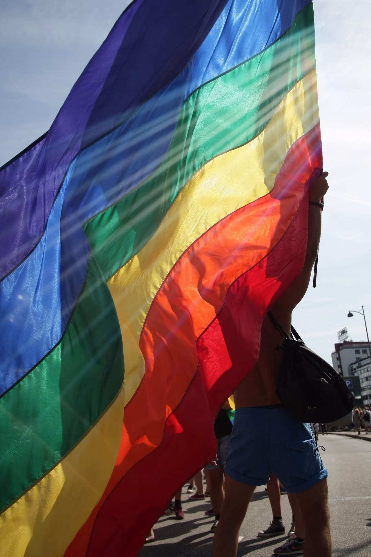 Vibrant rainbow flag waving at a lively pride parade on a sunny day.