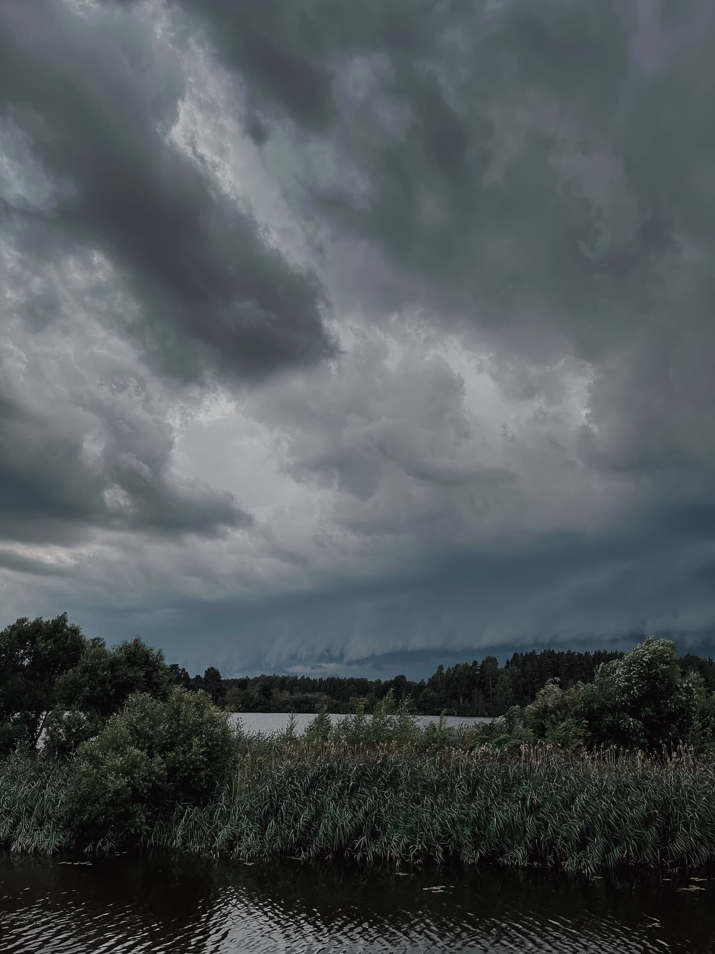 Storm clouds gather over a tranquil lake, creating a dramatic and moody landscape scene.
