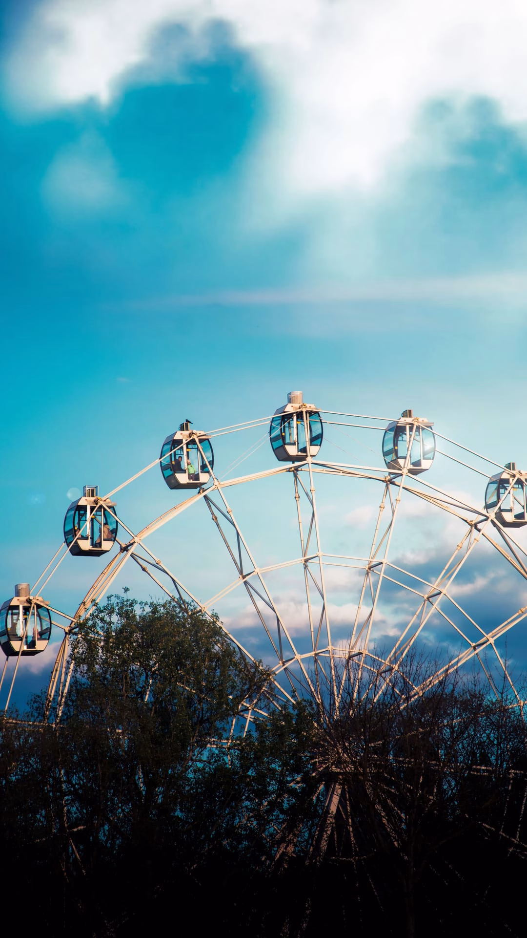 A large ferris wheel set against a vibrant blue sky with dramatic clouds.